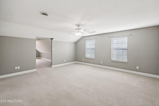 interior space with light colored carpet, visible vents, baseboards, vaulted ceiling, and a ceiling fan