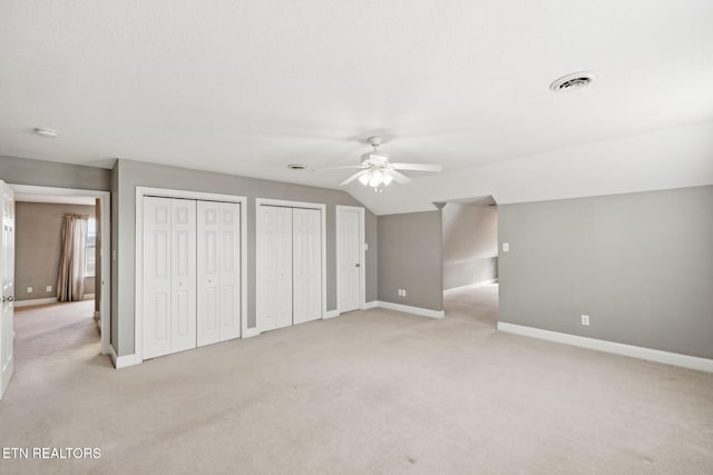 unfurnished bedroom featuring multiple closets, lofted ceiling, visible vents, light colored carpet, and baseboards