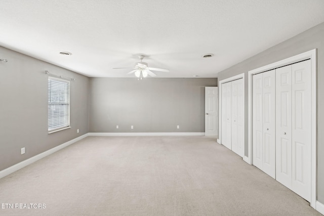 unfurnished bedroom with light carpet, baseboards, visible vents, and two closets
