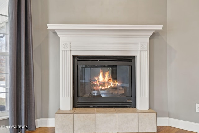 room details featuring a glass covered fireplace, baseboards, and wood finished floors