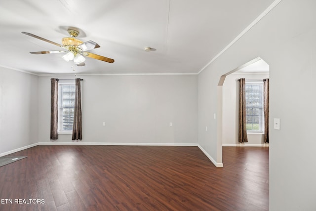 unfurnished room with baseboards, arched walkways, dark wood finished floors, and crown molding