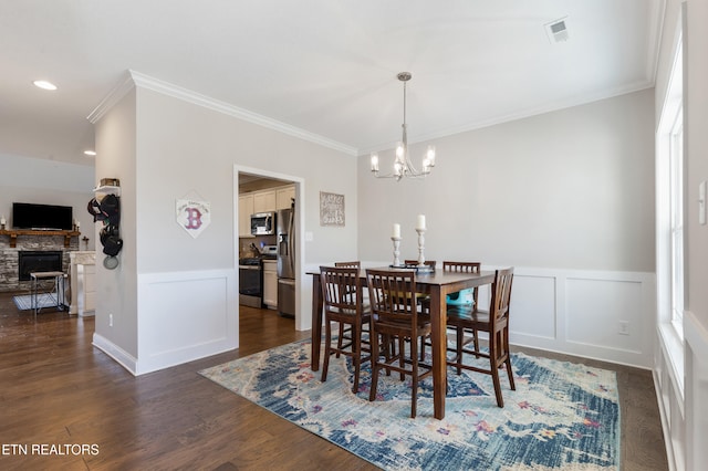 dining room with dark wood-type flooring, a fireplace, a chandelier, and crown molding