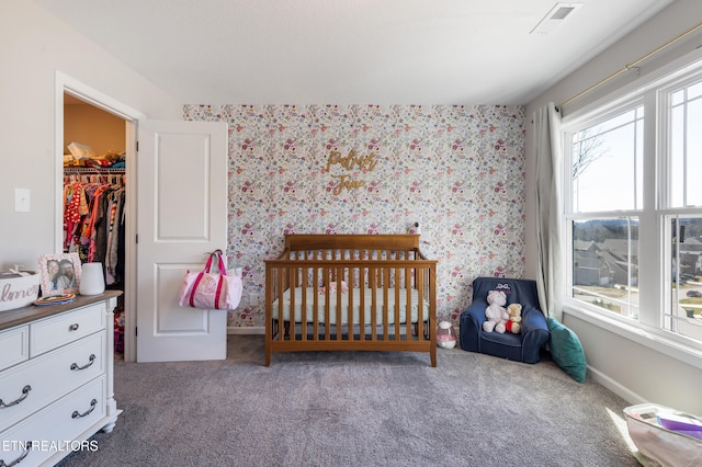 carpeted bedroom featuring a spacious closet and a crib