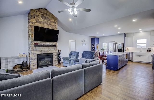 living room featuring french doors, light hardwood / wood-style flooring, a stone fireplace, sink, and ceiling fan