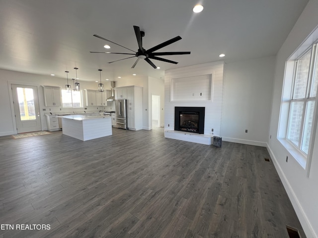 unfurnished living room featuring a fireplace, ceiling fan, and dark wood-type flooring