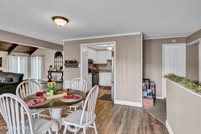 dining area featuring a textured ceiling, wood finished floors, baseboards, ornamental molding, and beam ceiling