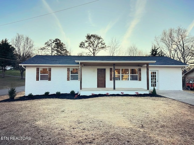 ranch-style house featuring covered porch, brick siding, and a front yard