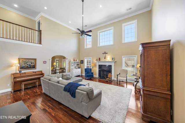 living room featuring visible vents, arched walkways, dark wood-style floors, crown molding, and a high end fireplace