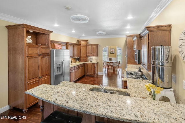 kitchen featuring arched walkways, light stone counters, a kitchen breakfast bar, a peninsula, and stainless steel appliances