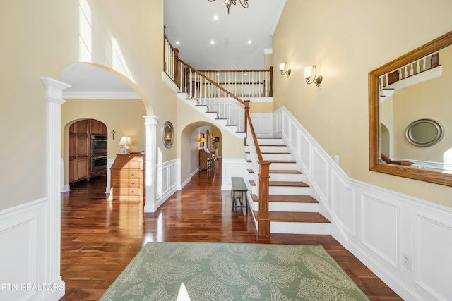 staircase with ornate columns, arched walkways, wood finished floors, and ornamental molding