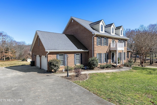 colonial-style house with a balcony, brick siding, a shingled roof, driveway, and a front lawn