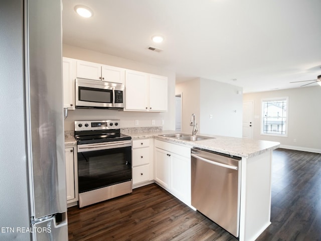 kitchen with appliances with stainless steel finishes, dark wood-type flooring, sink, white cabinetry, and kitchen peninsula