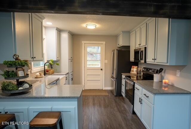 kitchen with dark wood finished floors, a breakfast bar area, appliances with stainless steel finishes, a peninsula, and a sink