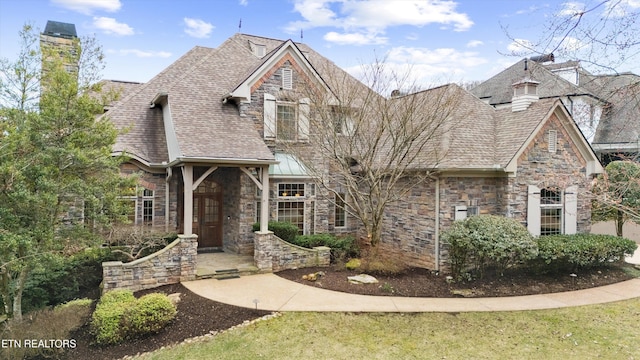 view of front of home featuring stone siding, a shingled roof, and a chimney