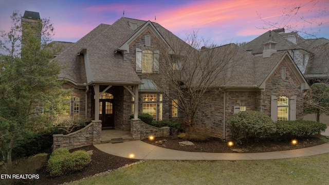 view of front facade with stone siding and a shingled roof