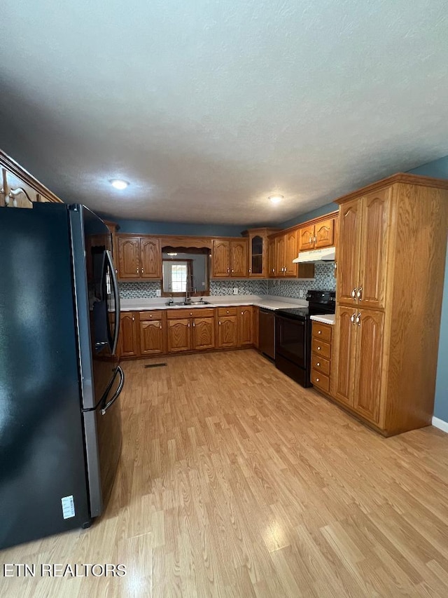 kitchen with brown cabinets, light wood finished floors, black / electric stove, under cabinet range hood, and freestanding refrigerator