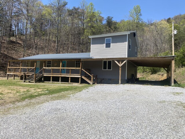 farmhouse-style home with a forest view, a porch, gravel driveway, and crawl space