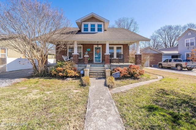 bungalow-style house featuring covered porch, fence, a front lawn, and brick siding