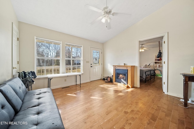 living area featuring visible vents, lofted ceiling, ceiling fan, wood finished floors, and a lit fireplace