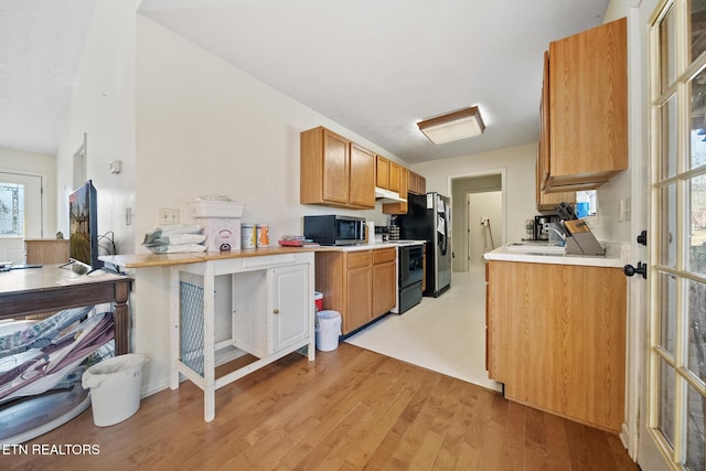 kitchen featuring stainless steel appliances, light countertops, brown cabinetry, light wood-style floors, and under cabinet range hood