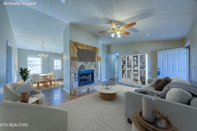 living area featuring lofted ceiling, a textured ceiling, ceiling fan with notable chandelier, a fireplace, and wood finished floors