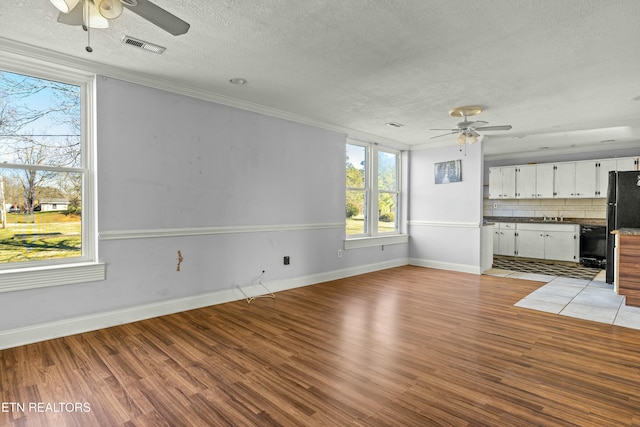 unfurnished living room featuring a textured ceiling, light wood finished floors, ornamental molding, and a ceiling fan