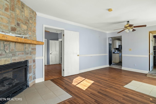 unfurnished living room featuring light wood finished floors, baseboards, ceiling fan, crown molding, and a stone fireplace