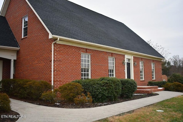 view of property exterior featuring brick siding and roof with shingles