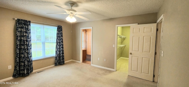 unfurnished bedroom featuring light colored carpet, ceiling fan, a walk in closet, and a textured ceiling