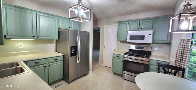 kitchen featuring stainless steel appliances, pendant lighting, green cabinets, and a textured ceiling