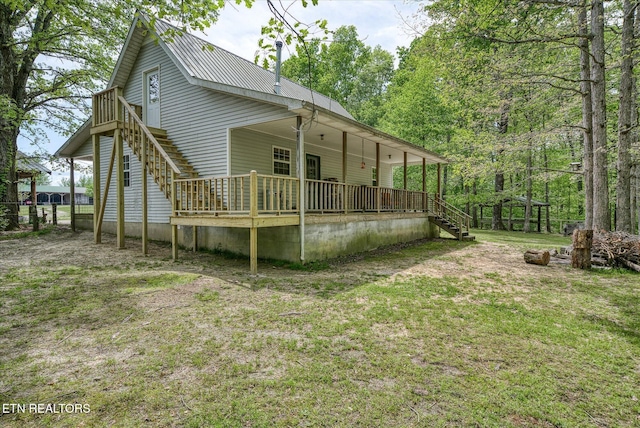 back of property featuring metal roof, a lawn, and stairs