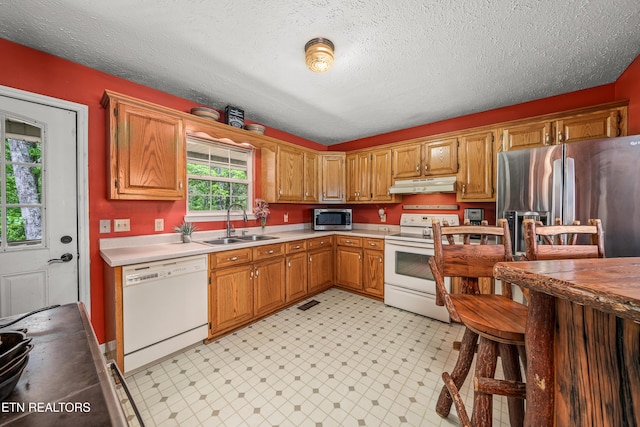 kitchen featuring brown cabinets, light countertops, appliances with stainless steel finishes, a sink, and under cabinet range hood