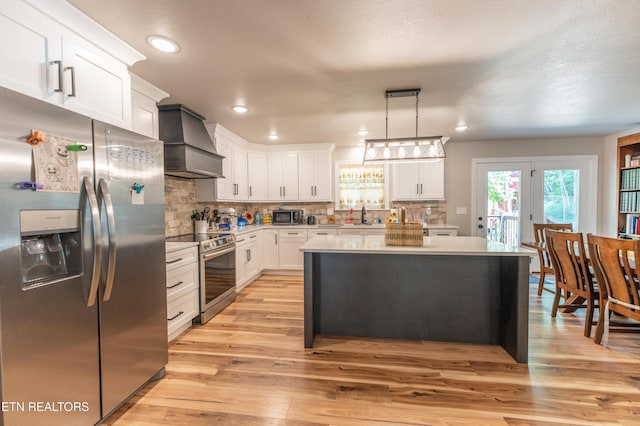 kitchen featuring appliances with stainless steel finishes, pendant lighting, custom range hood, a kitchen island, and white cabinets