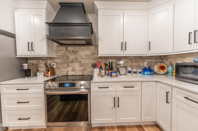 kitchen with stainless steel electric range, premium range hood, white cabinetry, and backsplash