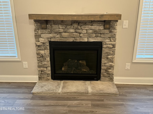 room details featuring a stone fireplace, baseboards, and wood finished floors