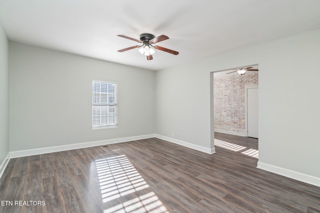 spare room featuring brick wall, wood finished floors, a ceiling fan, and baseboards