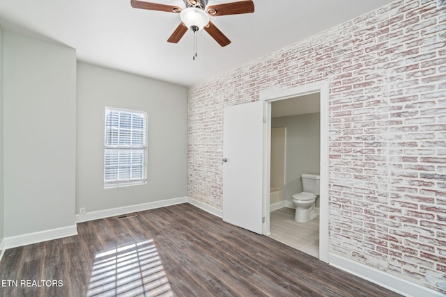 unfurnished bedroom featuring baseboards, connected bathroom, brick wall, and wood finished floors