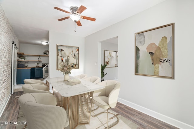 dining space with wood finished floors, baseboards, brick wall, and a barn door