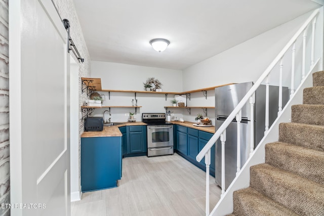 kitchen with a barn door, stainless steel appliances, a sink, blue cabinetry, and open shelves