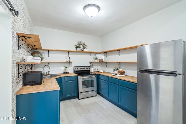 kitchen with blue cabinets, butcher block counters, a sink, appliances with stainless steel finishes, and open shelves