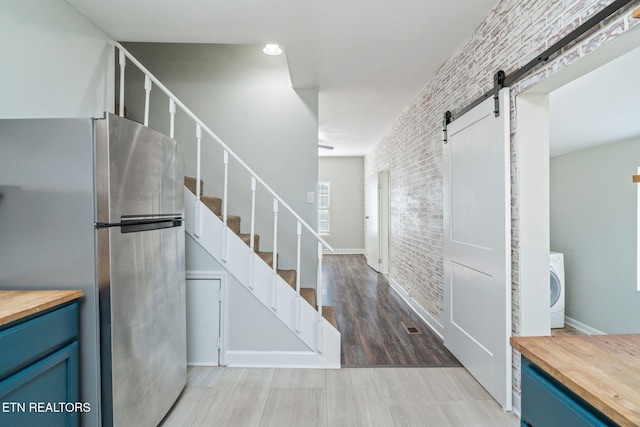 interior space featuring washer / clothes dryer, wood finished floors, brick wall, and a barn door