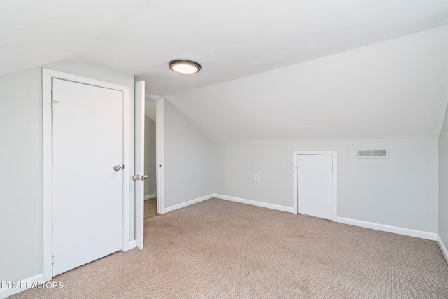 additional living space featuring light colored carpet, visible vents, lofted ceiling, and baseboards