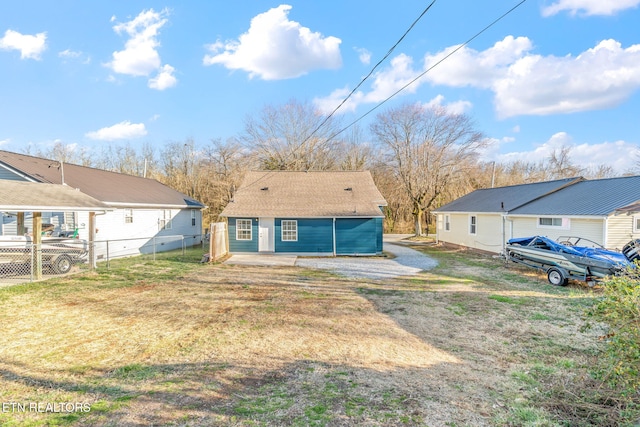 rear view of property featuring driveway, fence, and a lawn