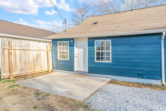 doorway to property featuring a patio area, a shingled roof, and fence