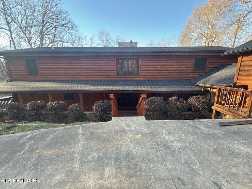 view of front facade featuring a shingled roof, log veneer siding, and a chimney