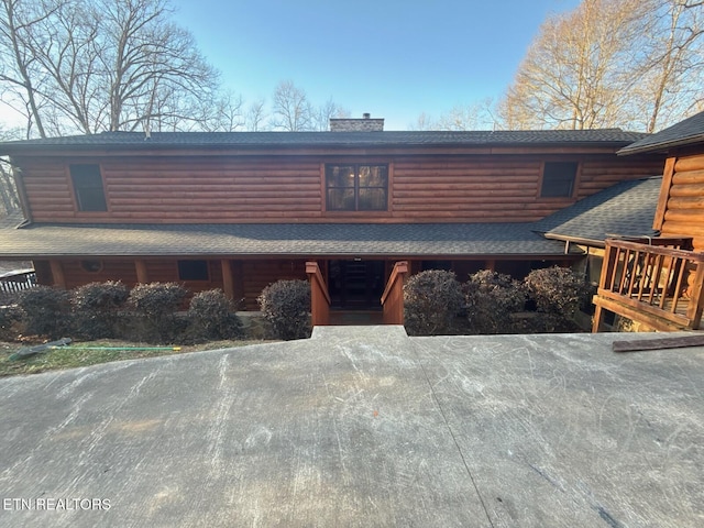 view of front facade featuring a shingled roof, log veneer siding, and a chimney