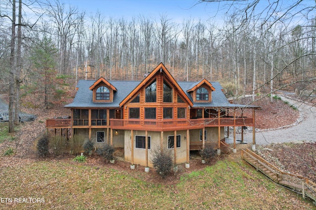 rear view of house featuring a wooden deck, a wooded view, log exterior, and stucco siding