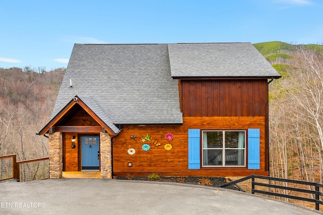 view of front facade featuring stone siding, roof with shingles, and fence