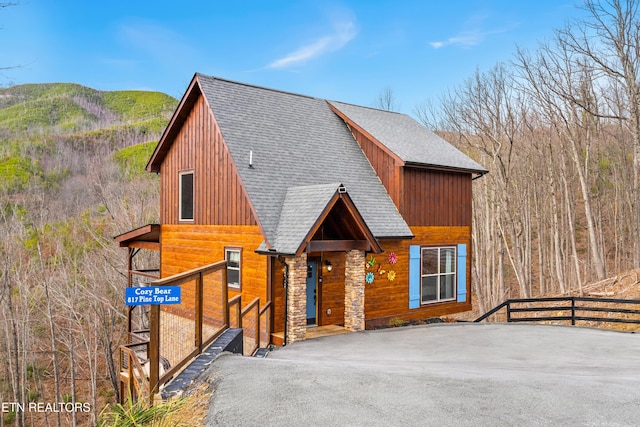 chalet / cabin featuring roof with shingles, board and batten siding, a mountain view, fence, and stone siding