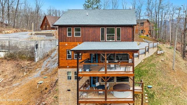 back of property with stone siding, roof with shingles, and a balcony